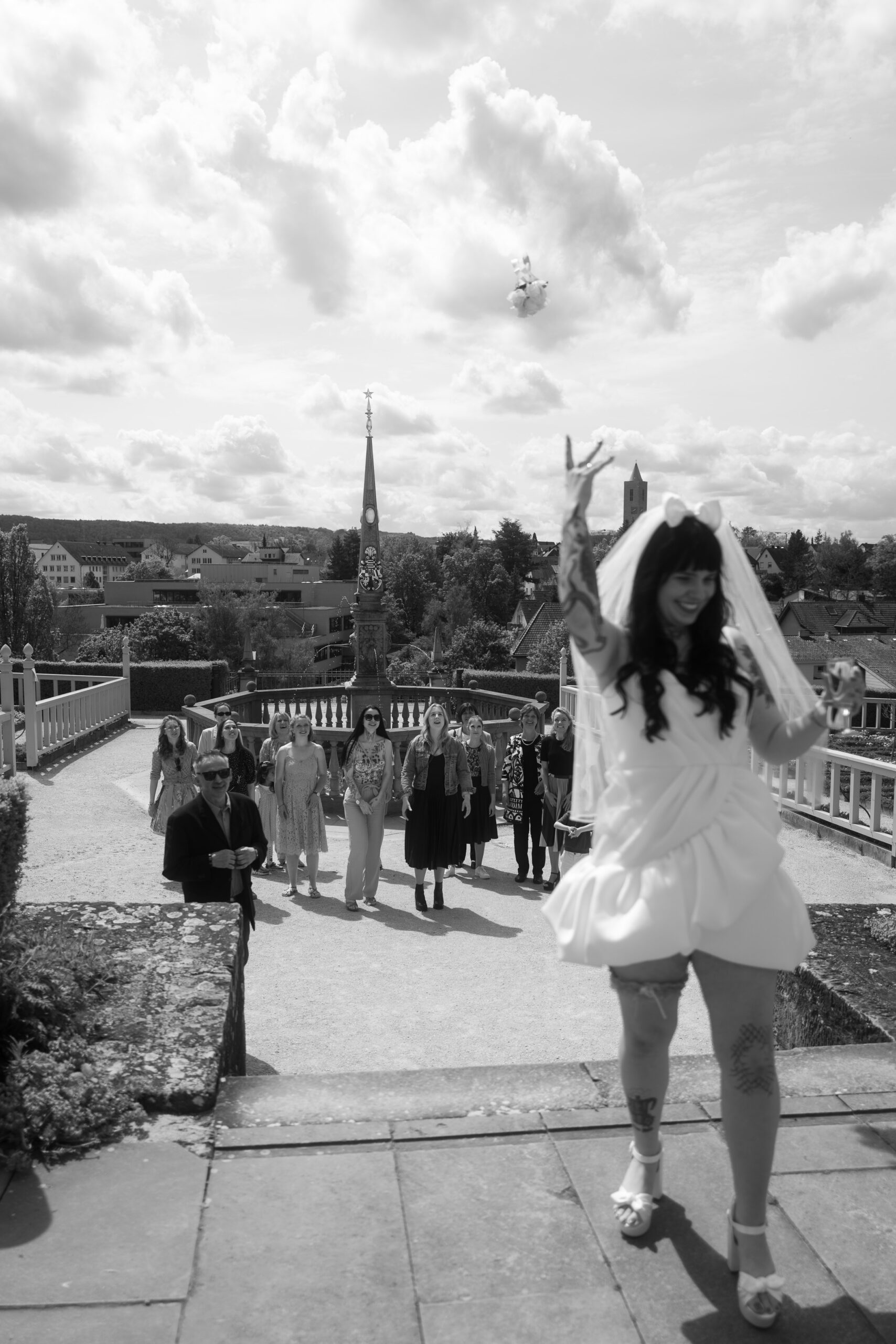 Braut wirft den Brautstrauß in die Luft, Hochzeitsgäste stehen lachend im Hintergrund, energiegeladene Hochzeitsfotografie.