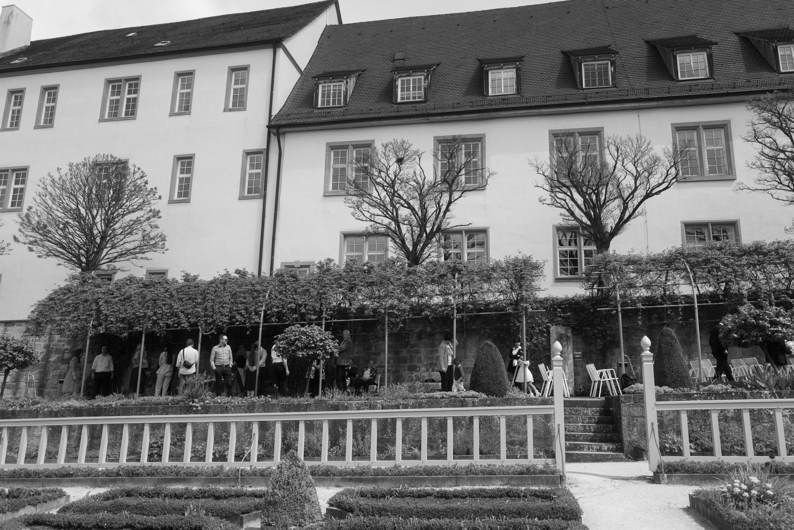 Hochzeitsgäste & Brautpaar in entspannter Atmosphäre, ungestellte Schwarz-Weiß-Aufnahme – alternative Hochzeitsfotografie.