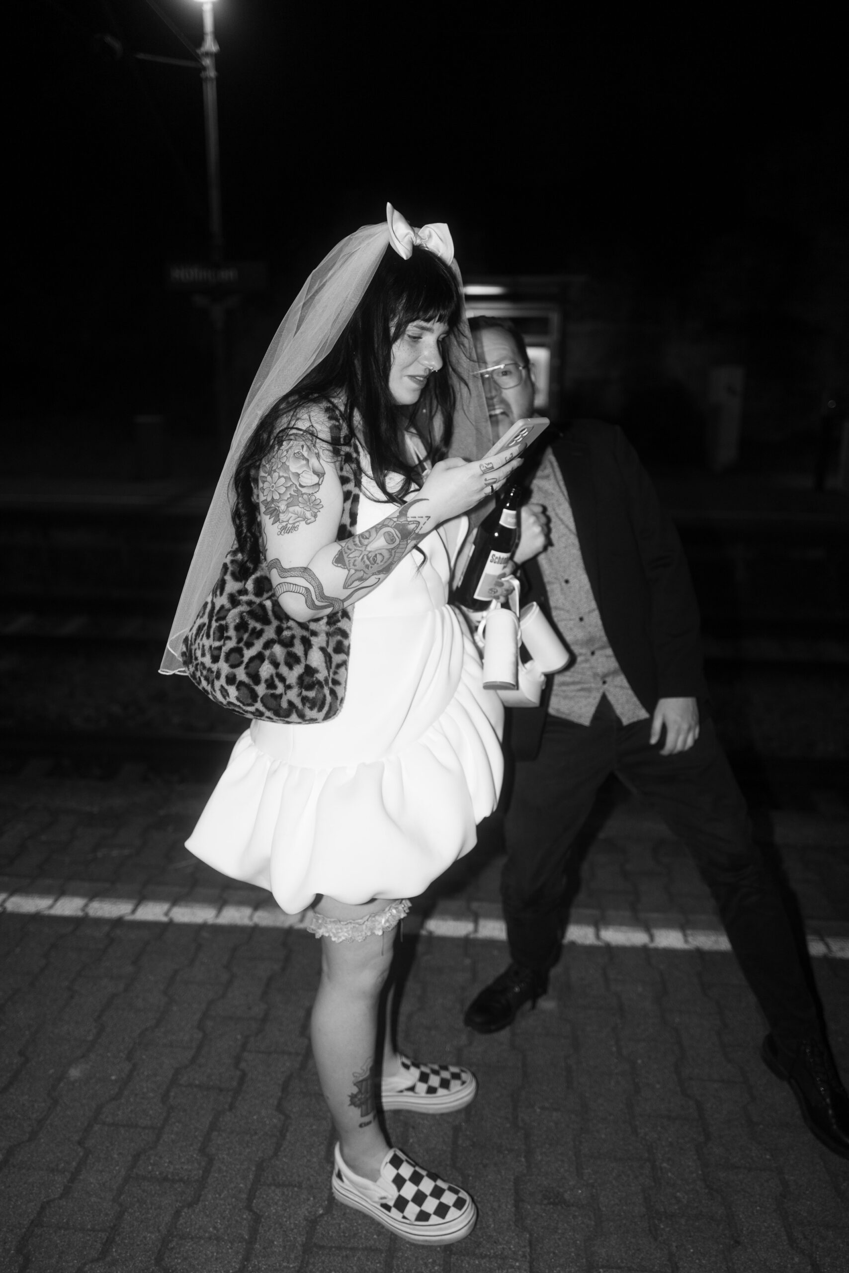 Unkonventionelle Braut mit Schleier, Vans & Mini-Kleid auf der Straße bei Nacht, wilde Hochzeit.