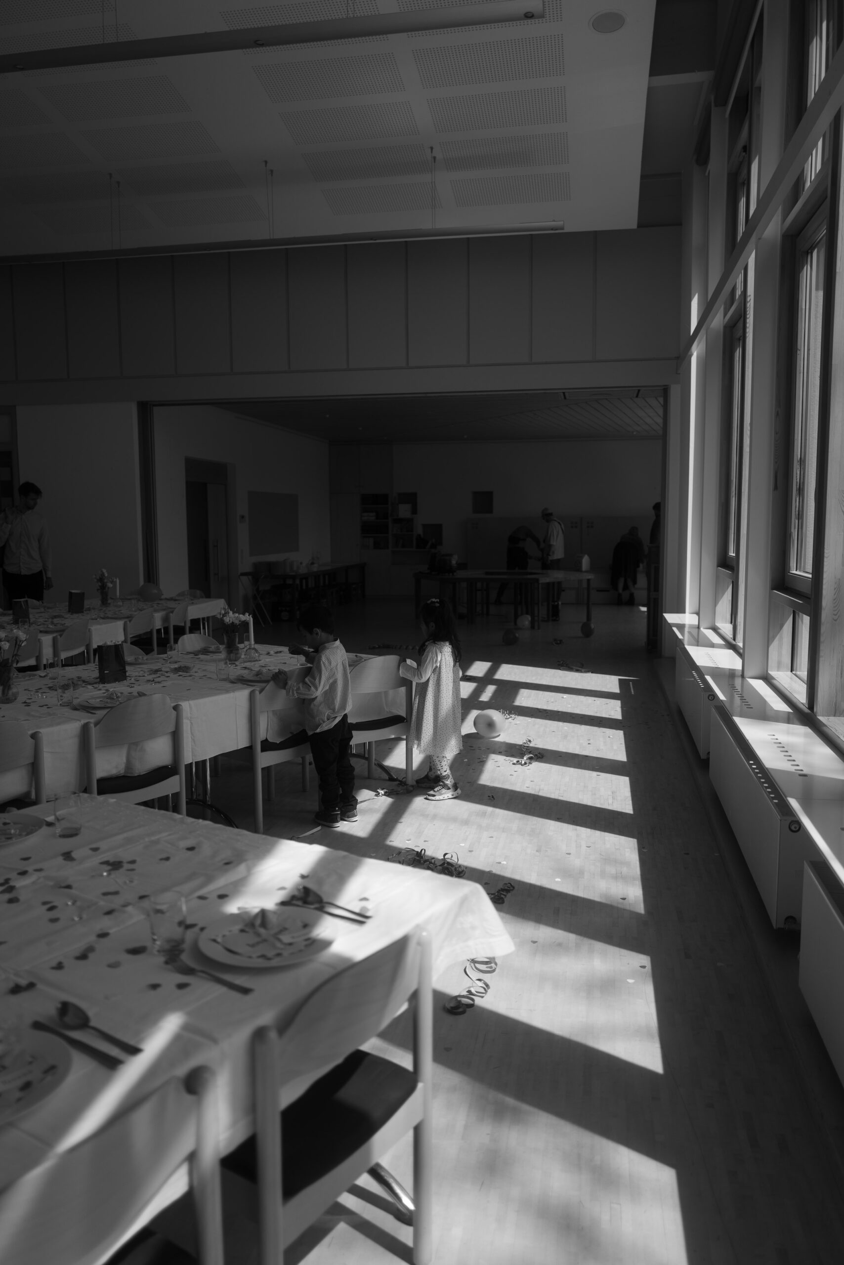 Sonnenlicht fällt durch die Fenster auf die Tische in einer leeren Hochzeitslocation – ruhige Atmosphäre vor der Feier.