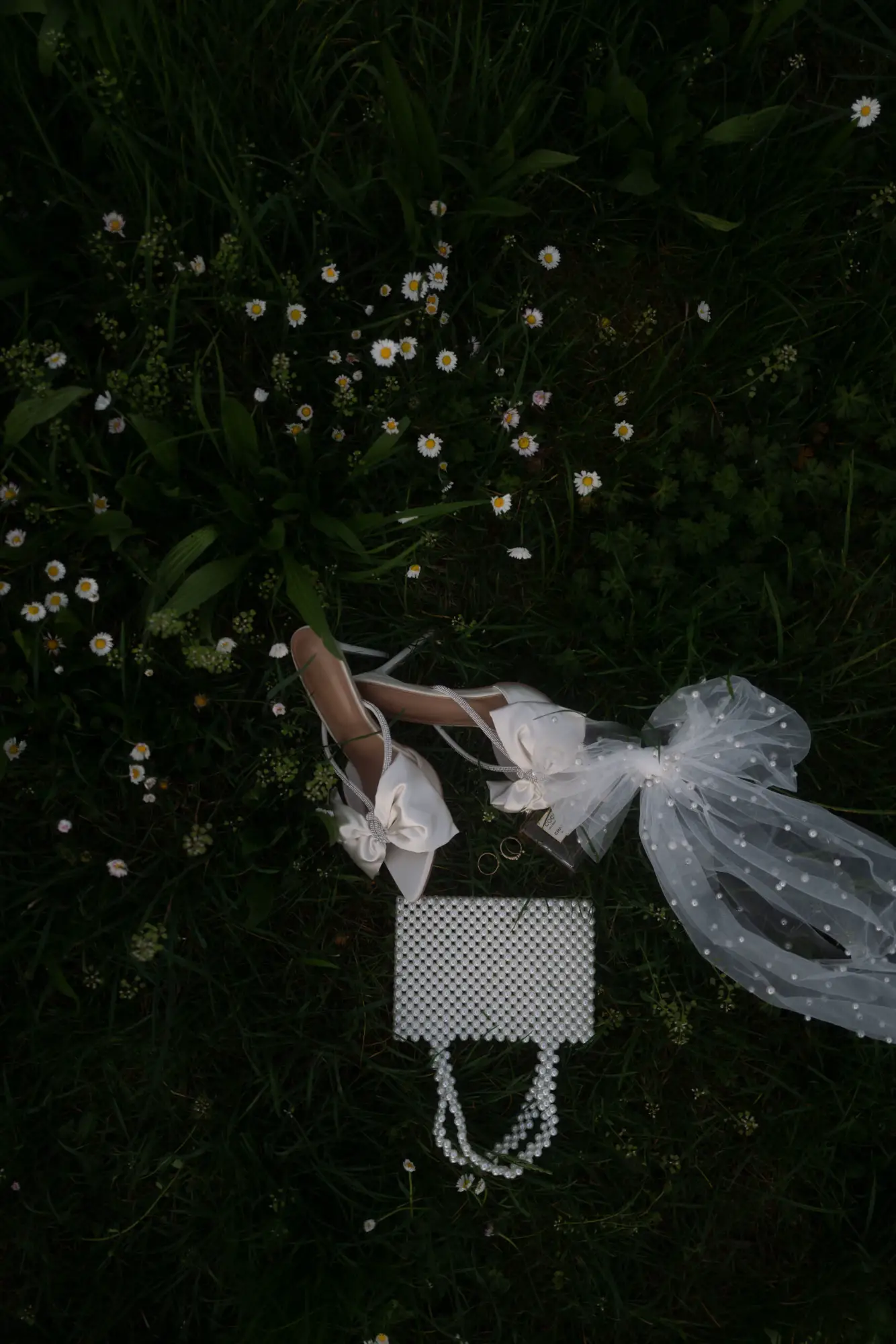 Brautschuhe, Schleier und Tasche liegen im Gras zwischen kleinen Gänseblümchen – moderne dokumentarische Hochzeitsfotografie mit Sinn für echte Emotionen und Details.