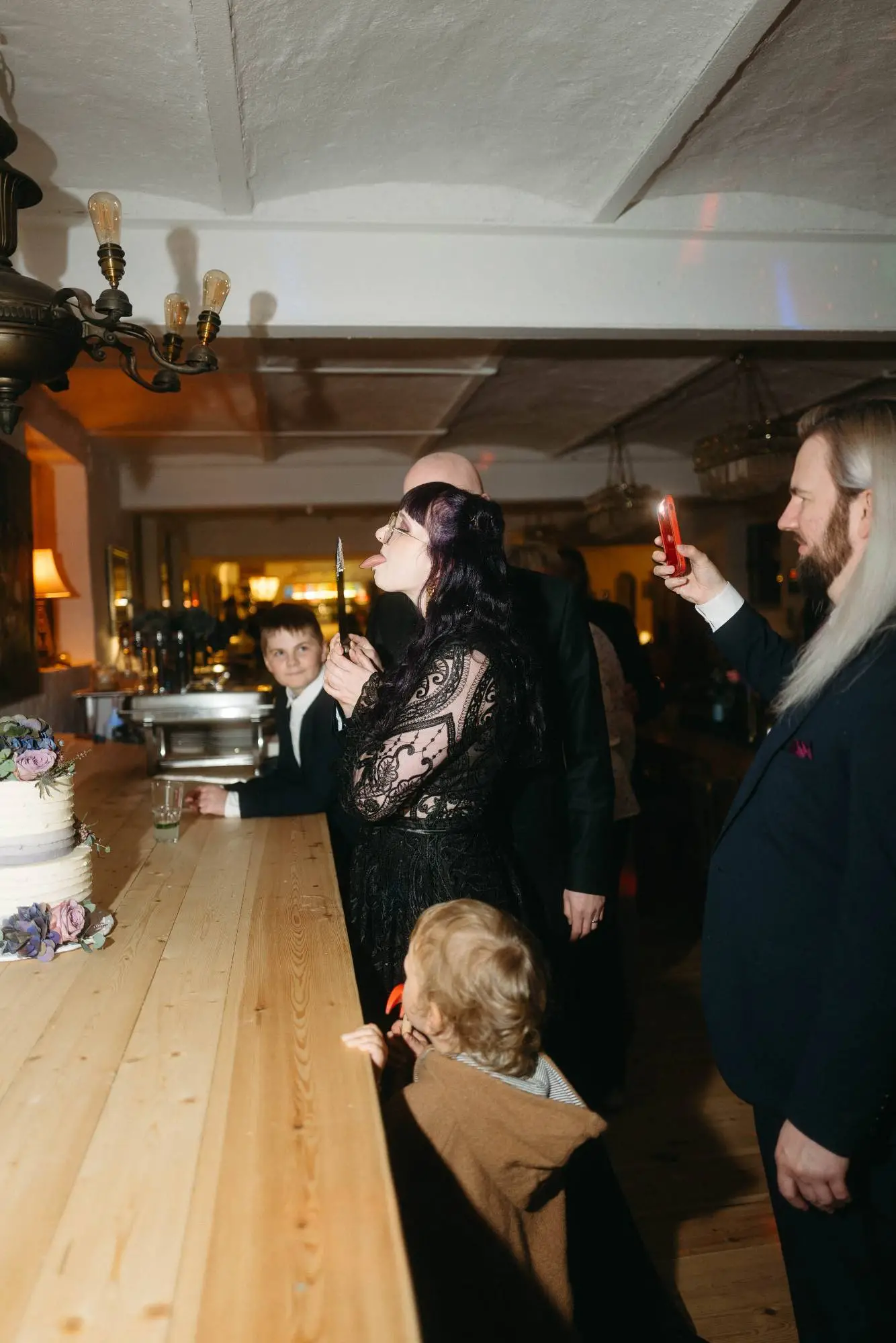 gäste in festlicher kleidung versammeln sich an der theke mit hochzeitstorte – moderne dokumentarische hochzeitsfotografie mit blick für intime momente und echte begegnungen