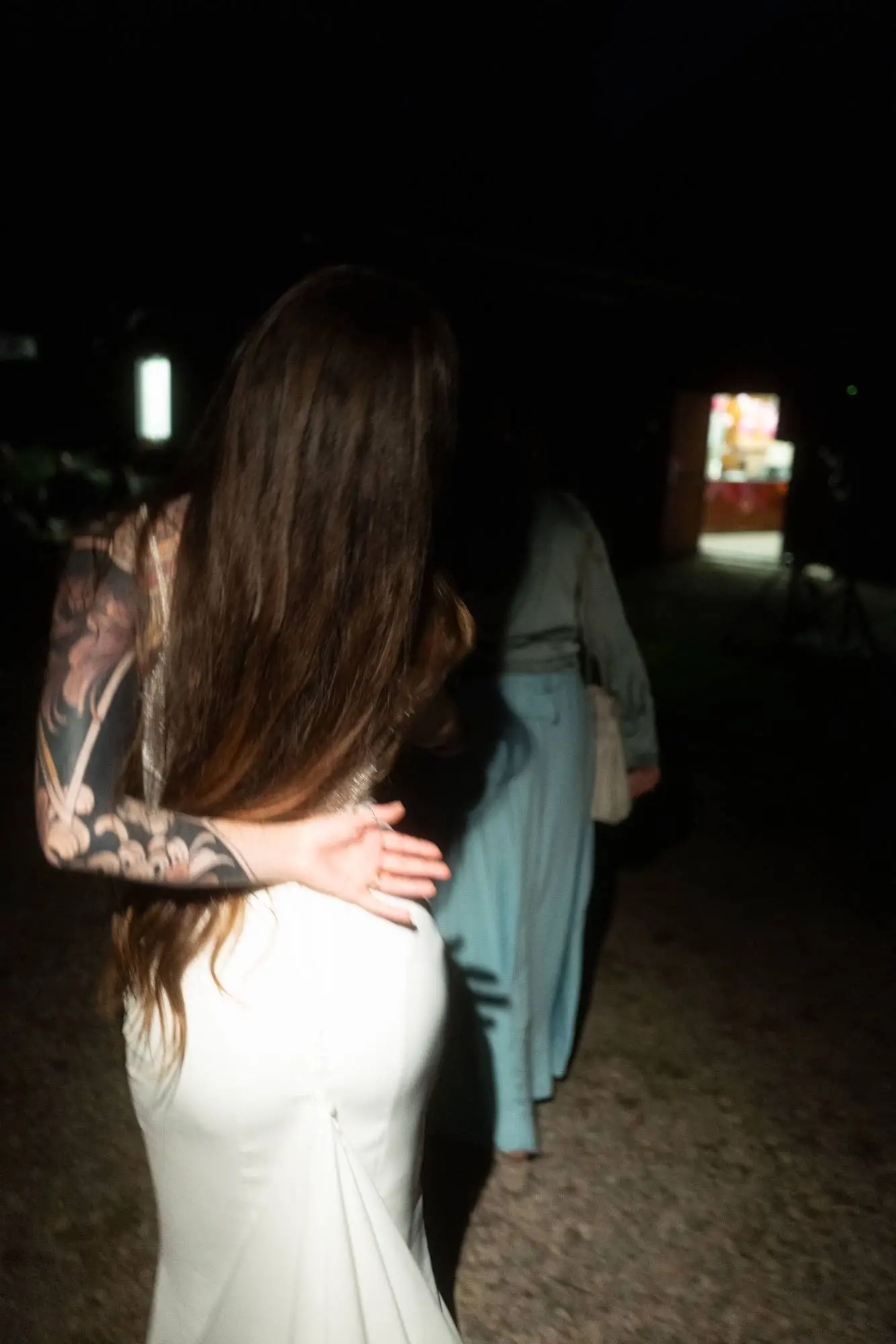 Intimer Moment bei Nacht: Braut in weißem Kleid wird liebevoll von einer tätowierten Person umarmt, Szene mit direktem Blitzlicht fotografiert.