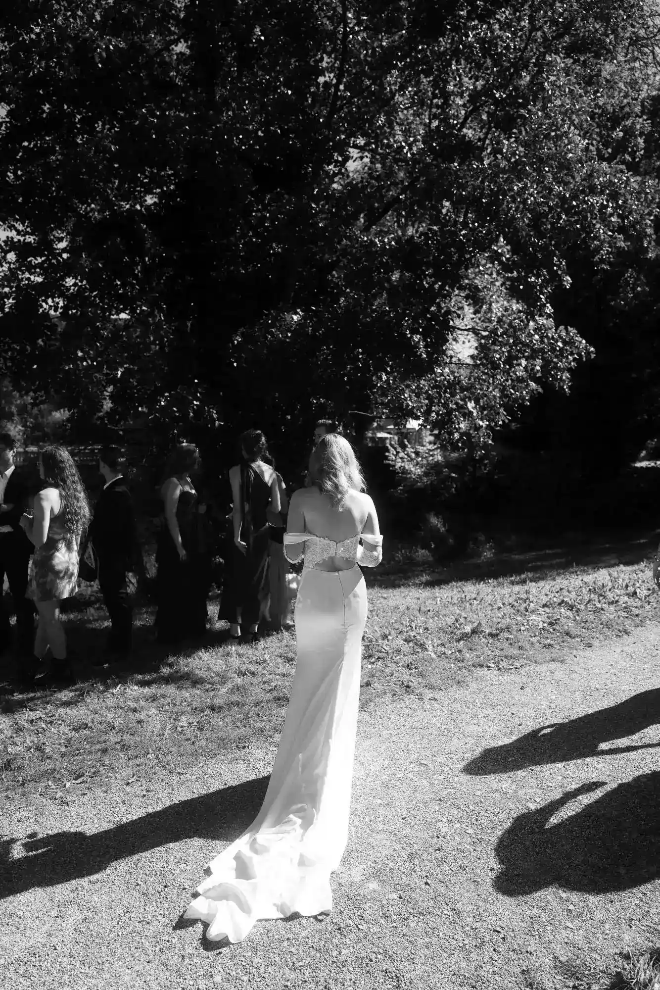 Moderne dokumentarische Hochzeitsfotografie – lebendige Szene mit der Braut im Sonnenlicht und Gästen im Hintergrund