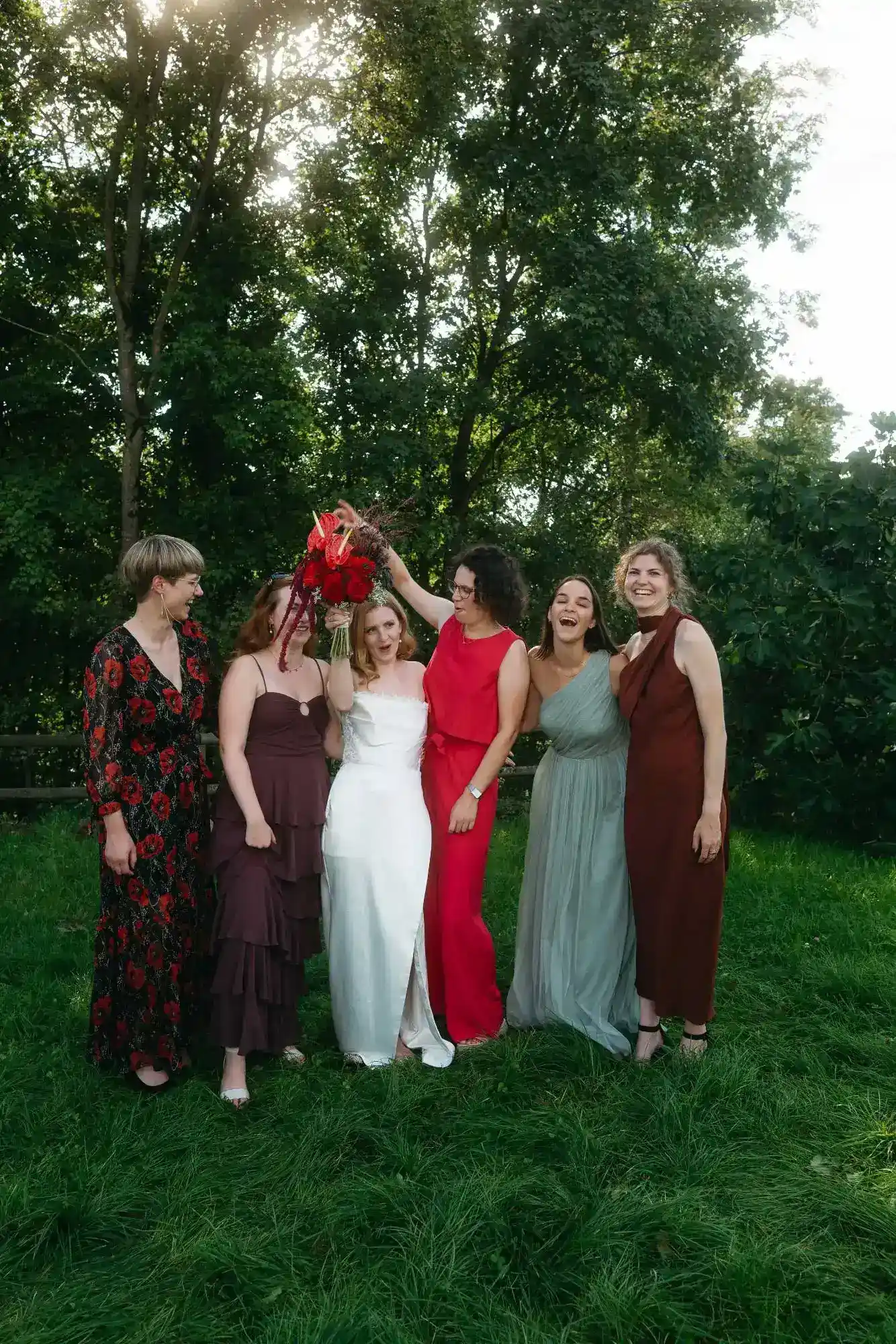 braut inmitten ihrer freundinnen hält den hochzeitsstrauß in die höhe – fröhlicher moment im garten bei natürlichem licht