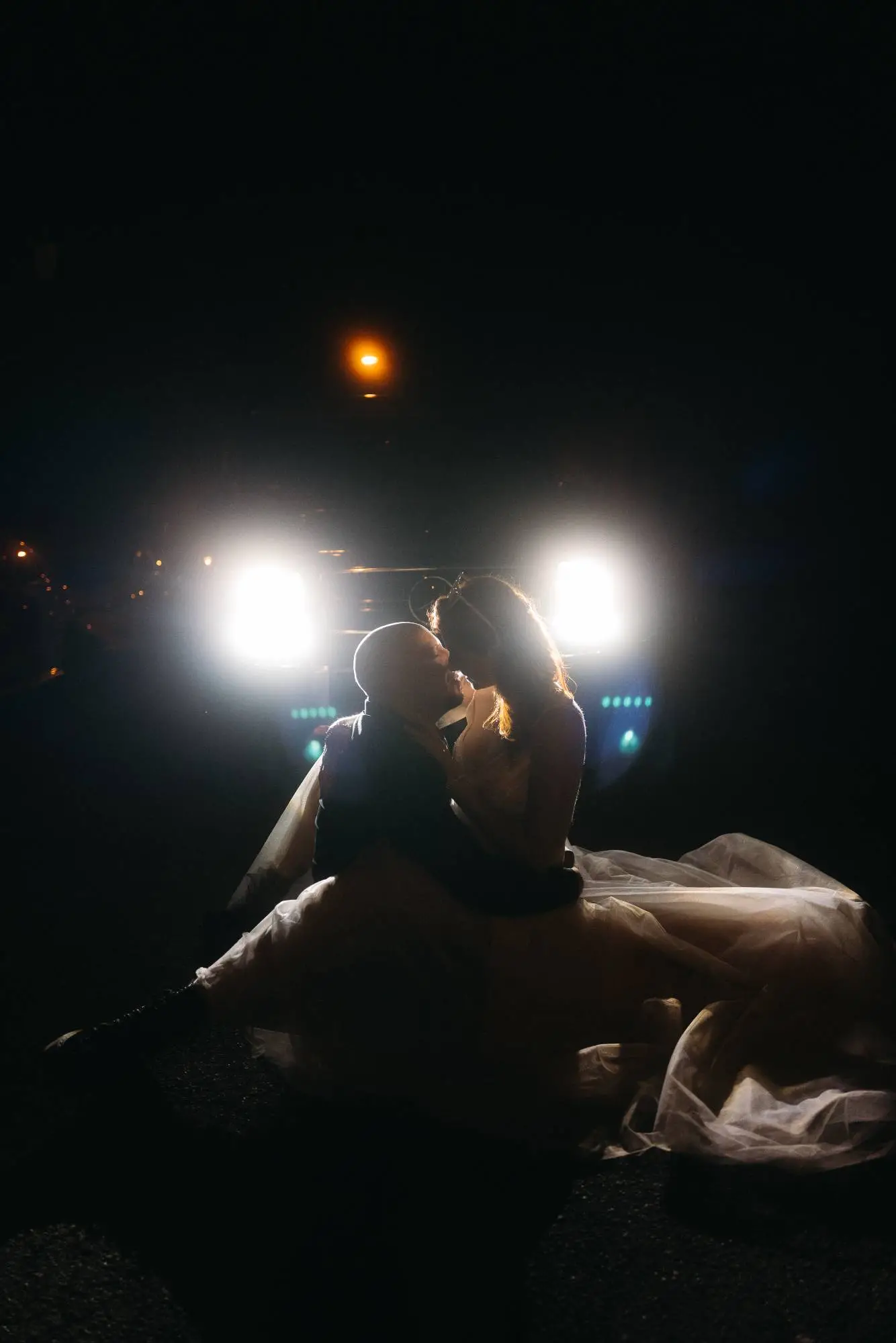 Hochzeitspaar küsst sich nachts vor Autoscheinwerfern – ein spontaner, emotionaler Moment in moderner dokumentarischer Hochzeitsfotografie.