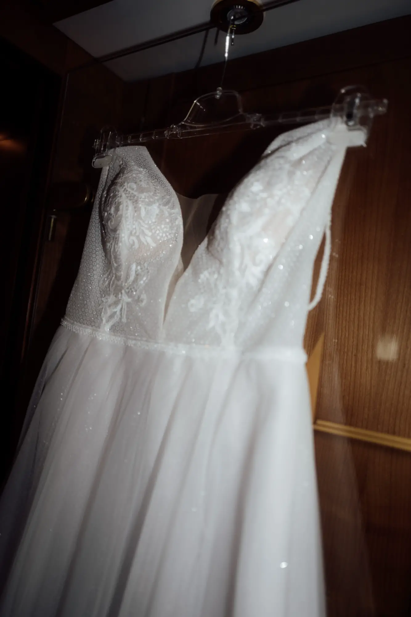 Hängendes Brautkleid mit Spitzenoberteil in warmer Holzumgebung, das auf seinen großen Moment wartet
