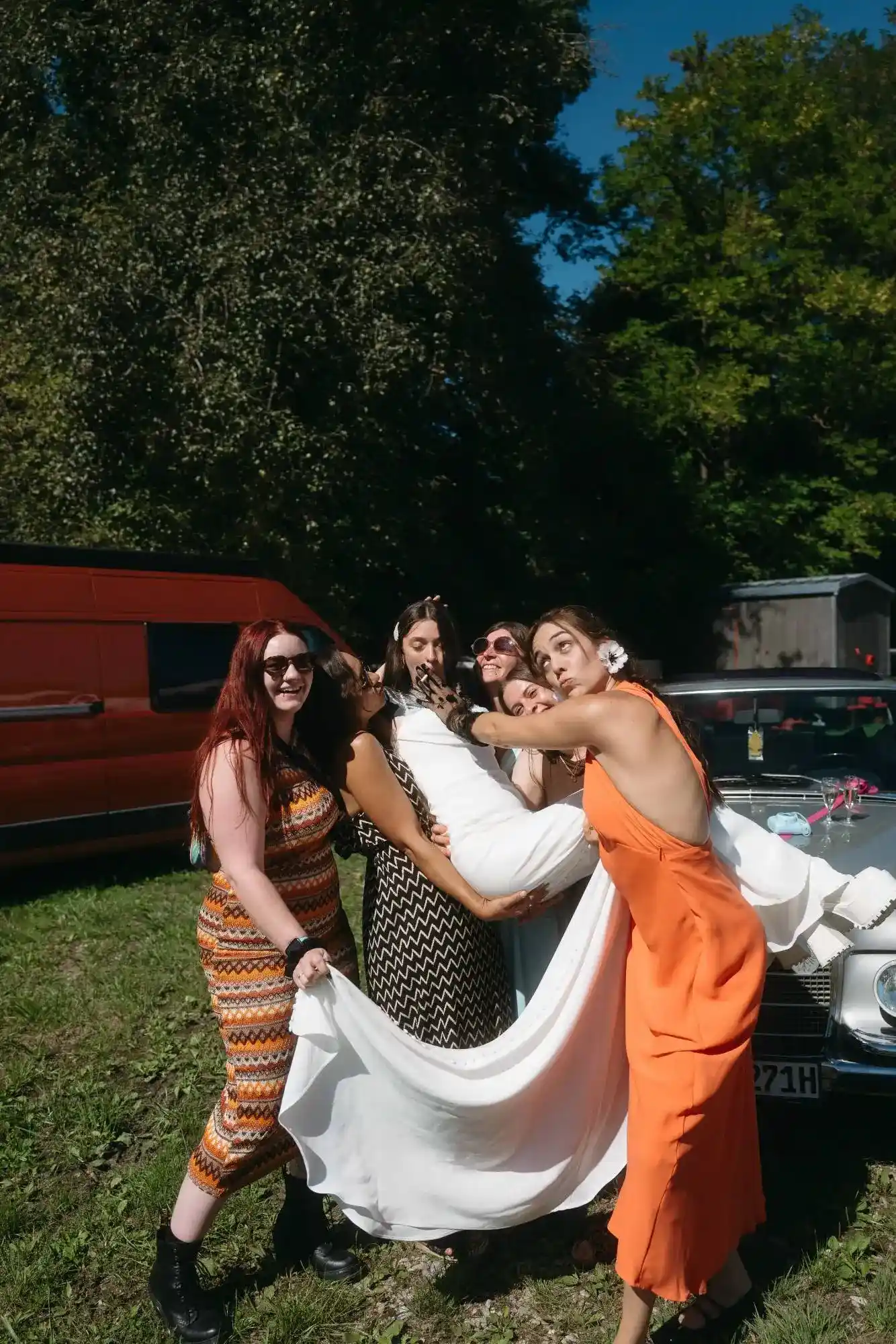 moderne dokumentarische hochzeitsfotografie mit freundinnen beim spaßigen moment des brautkleidtragens im freien