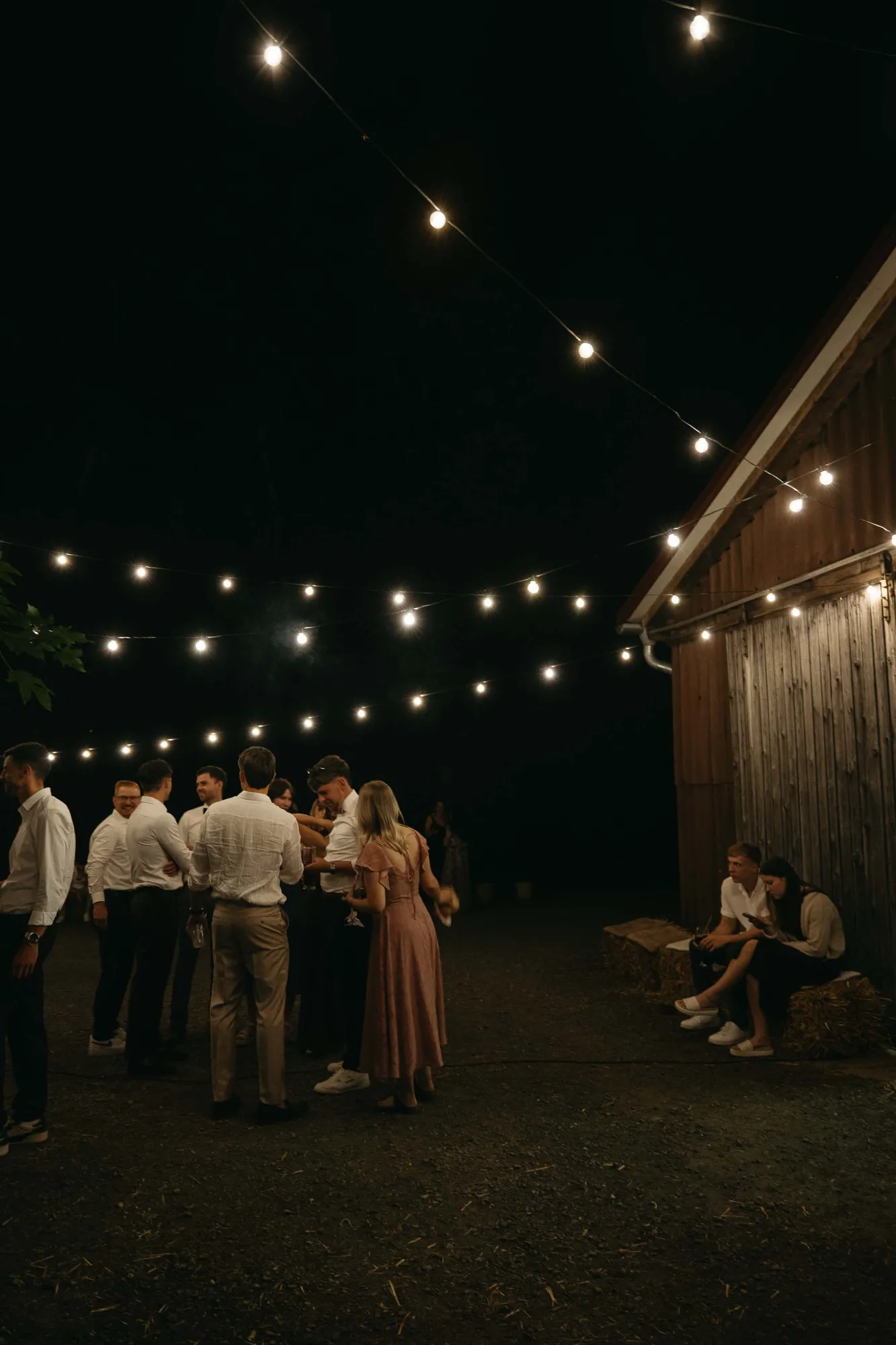 hochzeit-bewusst-geniessen Hochzeitsgäste verbringen gemeinsam Zeit unter Lichterketten am Abend.