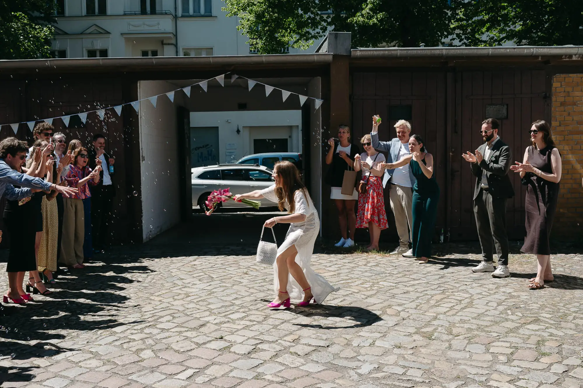 hochzeit-tante-frizzante-berlin-seifenblasen braut läuft mit pinkem brautstrauß durch seifenblasen und hochzeitsgäste bei der tante frizzante in berlin