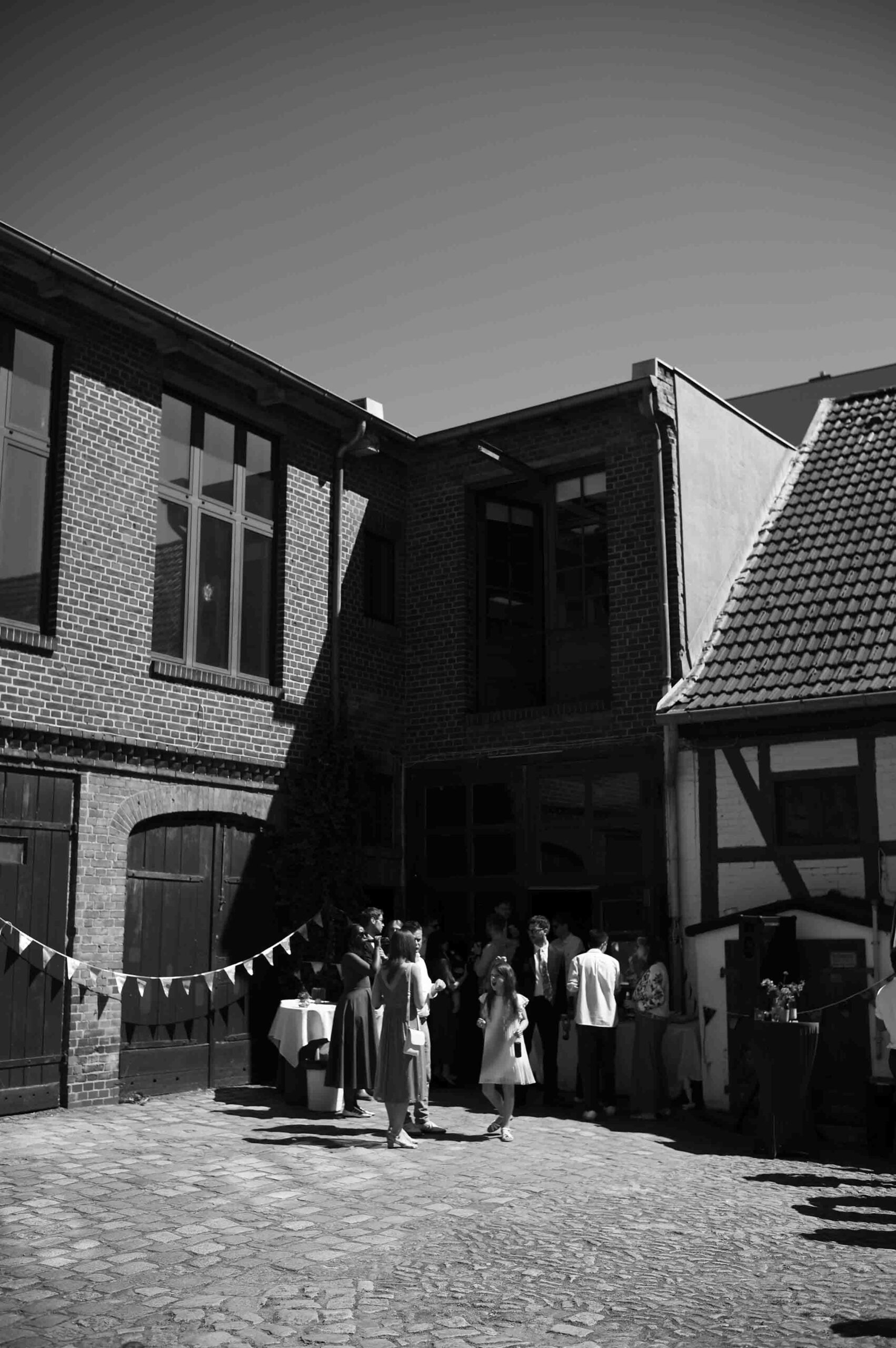 tante-frizzante-berlin-neukölln-hochzeit schwarzweißaufnahme der hochzeitslocation tante frizzante mit gästen im historischen innenhof in berlin-neukölln